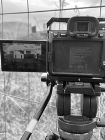 A camera on a tripod at a construction site — a building under construction visible on the screen and in the background